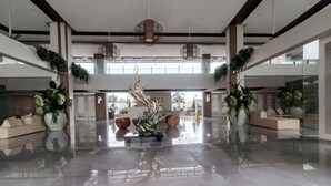 En rummelig lobby med slebet gulv, en central skulptur og potteplanter.
