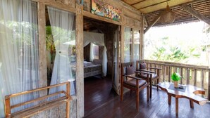 A rustic wooden room with a bed, a wooden chair, and a table with a plant. - Deluxe room with pool view at Ubud (Bali city)
