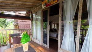 A wooden veranda with a table, a chair, and a bed visible through the glass doors. - Charming Deluxe room Upper floor at Ubud (Ubud)