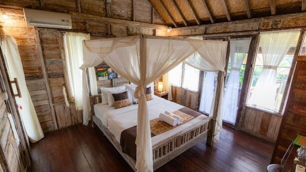 A rustic wooden room with a four-poster bed, a wooden floor, and a large window with curtains. - Charming Deluxe room Upper floor at Ubud (Ubud)
