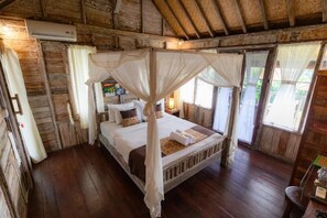 Une pièce rustique avec des murs en bois, un lit à baldaquin, un plancher en bois et une grande fenêtre ornée de rideaux.