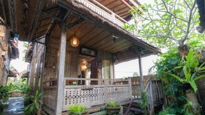 A traditional wooden house with a balcony, potted plants, and a thatched roof.