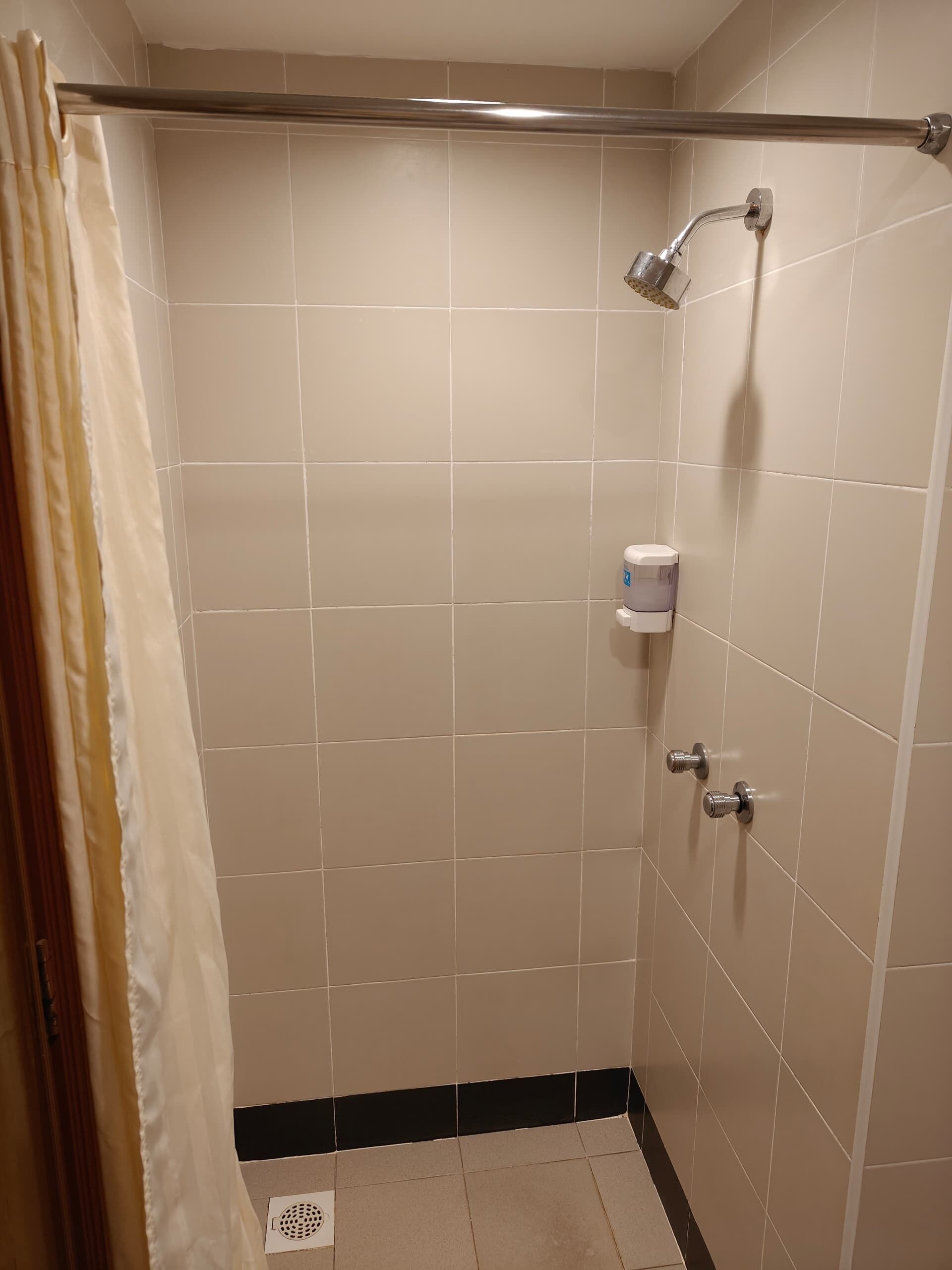 A small, tiled shower area with a showerhead, a towel dispenser, and a drain.