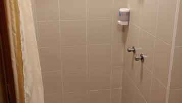 A small, tiled shower area with a showerhead, a towel dispenser, and a drain.