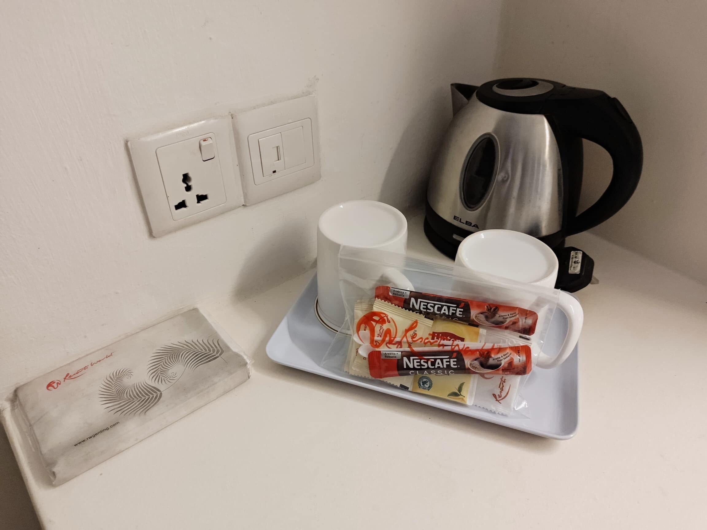 A kitchenette with a kettle, two cups, and a tray with Nescafe coffee packets.