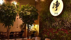 Un restaurant avec des tables et des chaises en bois, un long comptoir doté d’éviers, et un mur orné de plantes vertes et de fleurs.