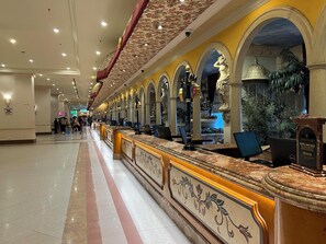 Un vestíbulo de hotel con un mostrador de recepción alargado, varios arcos y un techo decorativo.