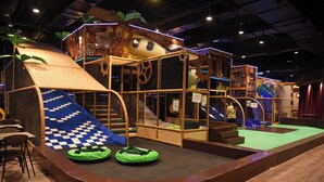 Un espace de jeux intérieur avec un toboggan, des structures d’escalade et une petite piscine.