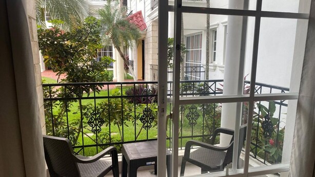 Een balkon met twee stoelen en een tafel, met uitzicht op een verzorgde tuin en een gebouw met balkons.