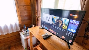 A wooden TV stand with a flat-screen TV displaying YouTube content, a remote control, and a small refrigerator. - Deluxe room upper floor with pool & nature view (Bali)