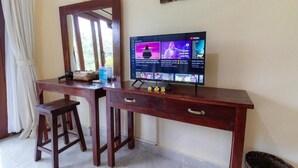 Puisesta pöydästä, jonka päällä on televisio, jossa näkyy useita eri kanavia, sekä peili ja pieni jakkara.