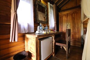 Interior de una cabaña de madera con un mostrador de madera, un refrigerador pequeño y una silla.