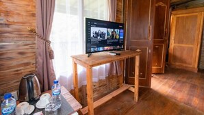 Una habitación de madera con una televisión sobre una mesa de madera, un hervidor y botellas de agua.