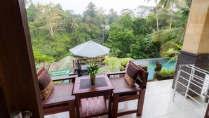 A balcony with wooden furniture and a view of a lush garden and a pool. - Tranquil Poolside Retreat (Tegallalang)