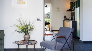 Een moderne woonkamer met een grijze fauteuil, een klein rond tafeltje met een bloevas, en een lijst met een foto aan de muur.