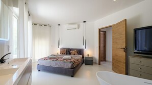 Een moderne slaapkamer met een groot bed, een ingebouwde televisie, een badkuip en een inloopkast.