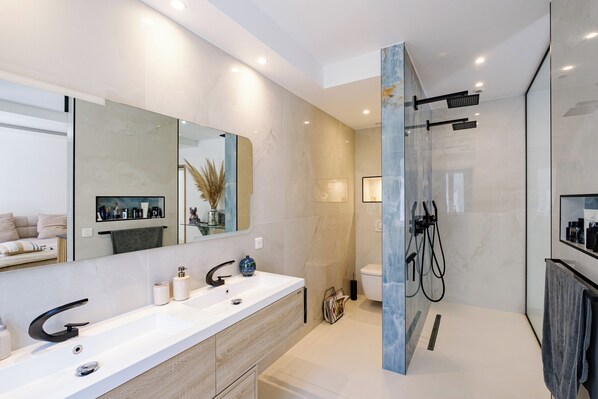 A modern bathroom with a large mirror, dual sinks, and a walk-in shower. - Luxury villa, gated community in Domène (Grimaud)