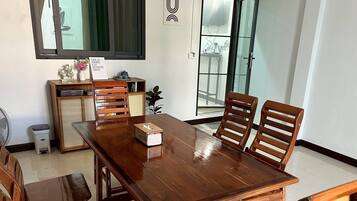 Een eetgedeelte met een houten tafel, vier stoelen, een bijzettafeltje met decoratieve objecten en een schuifdeur naar een balkon.