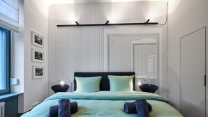 A neatly made bed with a headboard, two bedside lamps, and a wall with a geometric pattern. - Studio | Old Town | seeglueck (Konstanz)