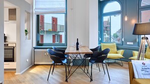 A modern kitchen with a built-in oven, a dining area with a wooden table and black chairs, and large windows with city views. - Studio | Old Town | seeglueck (Konstanz)