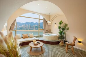 A room with a large arched window, a round bathtub, a seating area with cushions, a small round table, and a chair. - Chongqing City Center River View B&B (Chongqing)