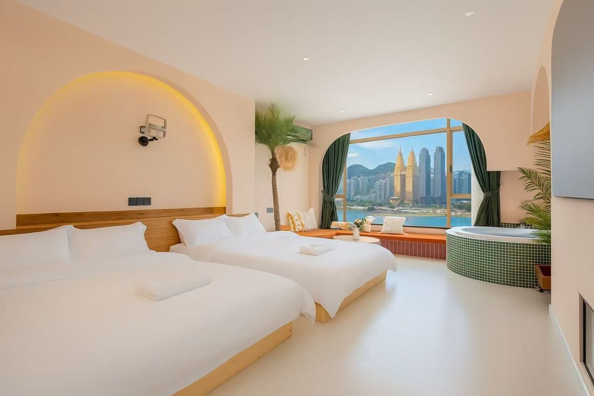 A hotel room with two beds, a view of a cityscape, a bathtub, and a window with curtains.