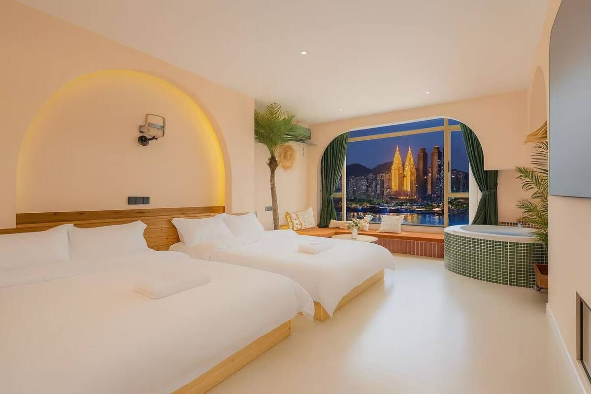 Ein Hotelzimmer mit zwei Betten, Blick auf eine Stadtansicht, einem kleinen Tisch und einer Badewanne.