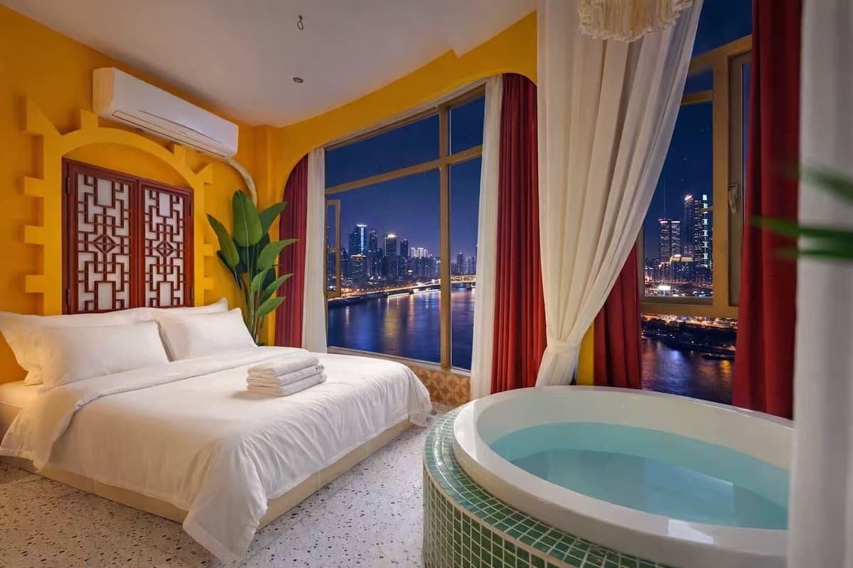 Ein Hotelzimmer mit Bett, Badewanne und Blick auf die Stadt bei Nacht.