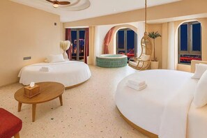 Quarto de hotel com duas camas, uma mesinha redonda, uma cadeira, uma mesinha de apoio com lenços de papel e vista para a cidade à noite.