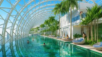 Una piscina interior moderna con techo de vidrio, palmeras y zonas de descanso.