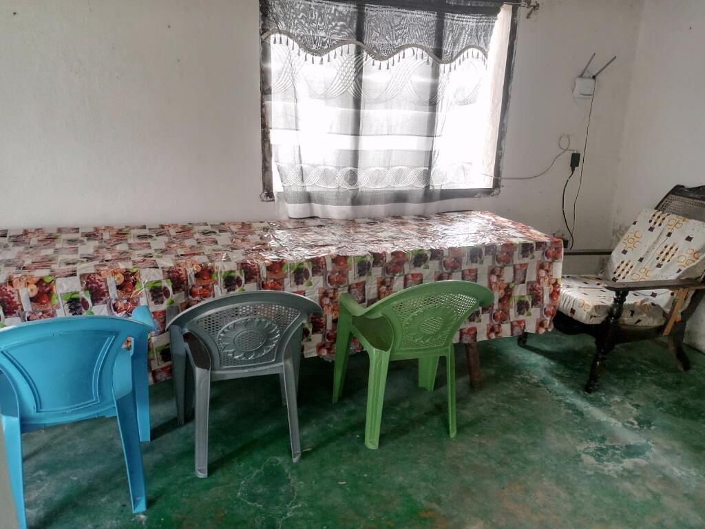Una habitación con una cama cubierta por una colcha de estampado floral, una ventana con cortinas de encaje y un piso verde.