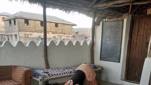 Uma pessoa fazendo uma postura de yoga em um tapete, num quarto com um banco de madeira, um sofá e uma parede com um quadro negro.