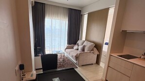 Ett kompakt bostadsutrymme med ett litet kök, en soffa, ett matbord och utsikt genom ett stort fönster.