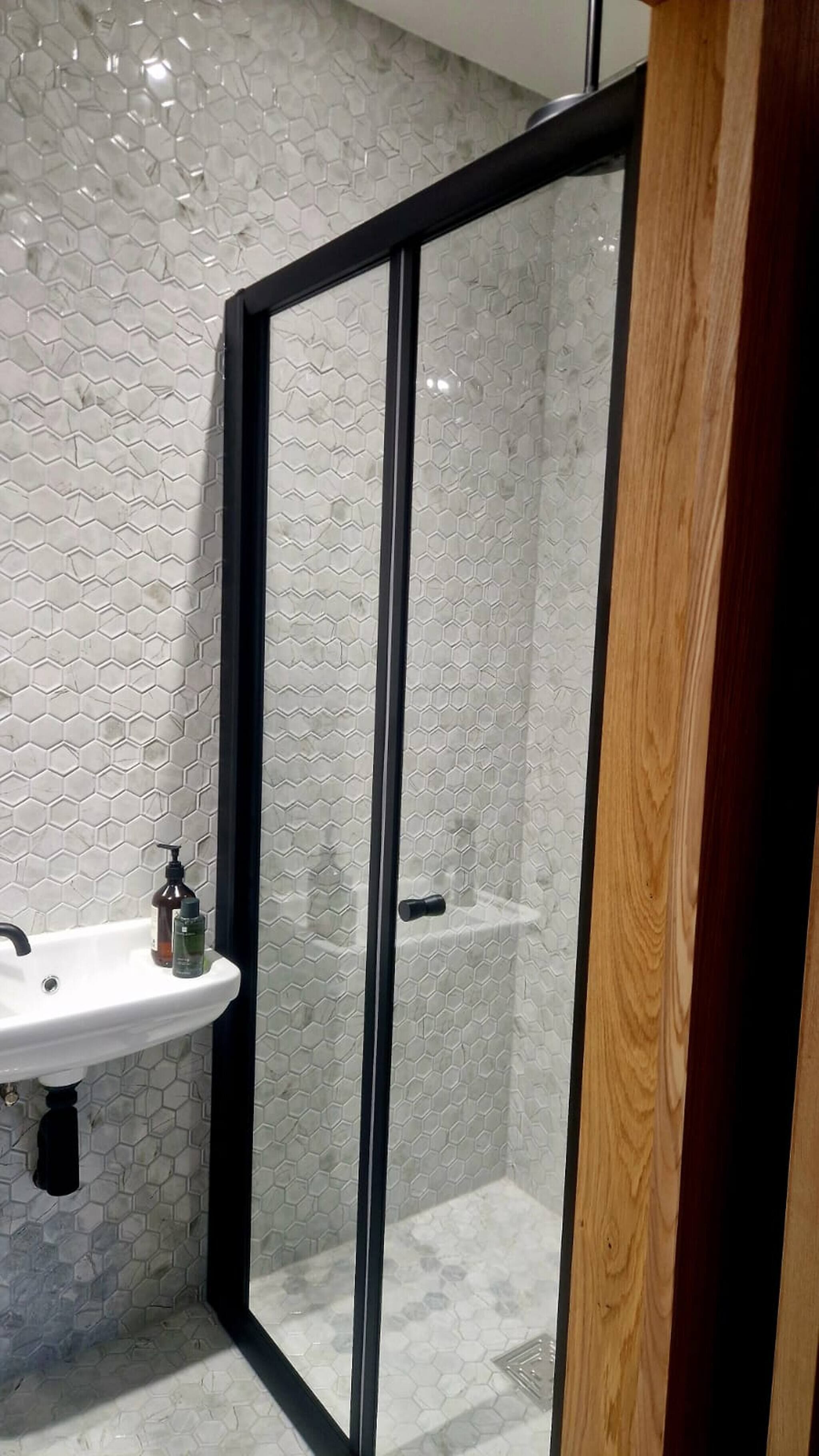Ein modernes Badezimmer mit Duschkabine aus Glas, einem weißen Waschbecken mit Pflegeprodukten und einer Wand mit sechseckigem Muster.