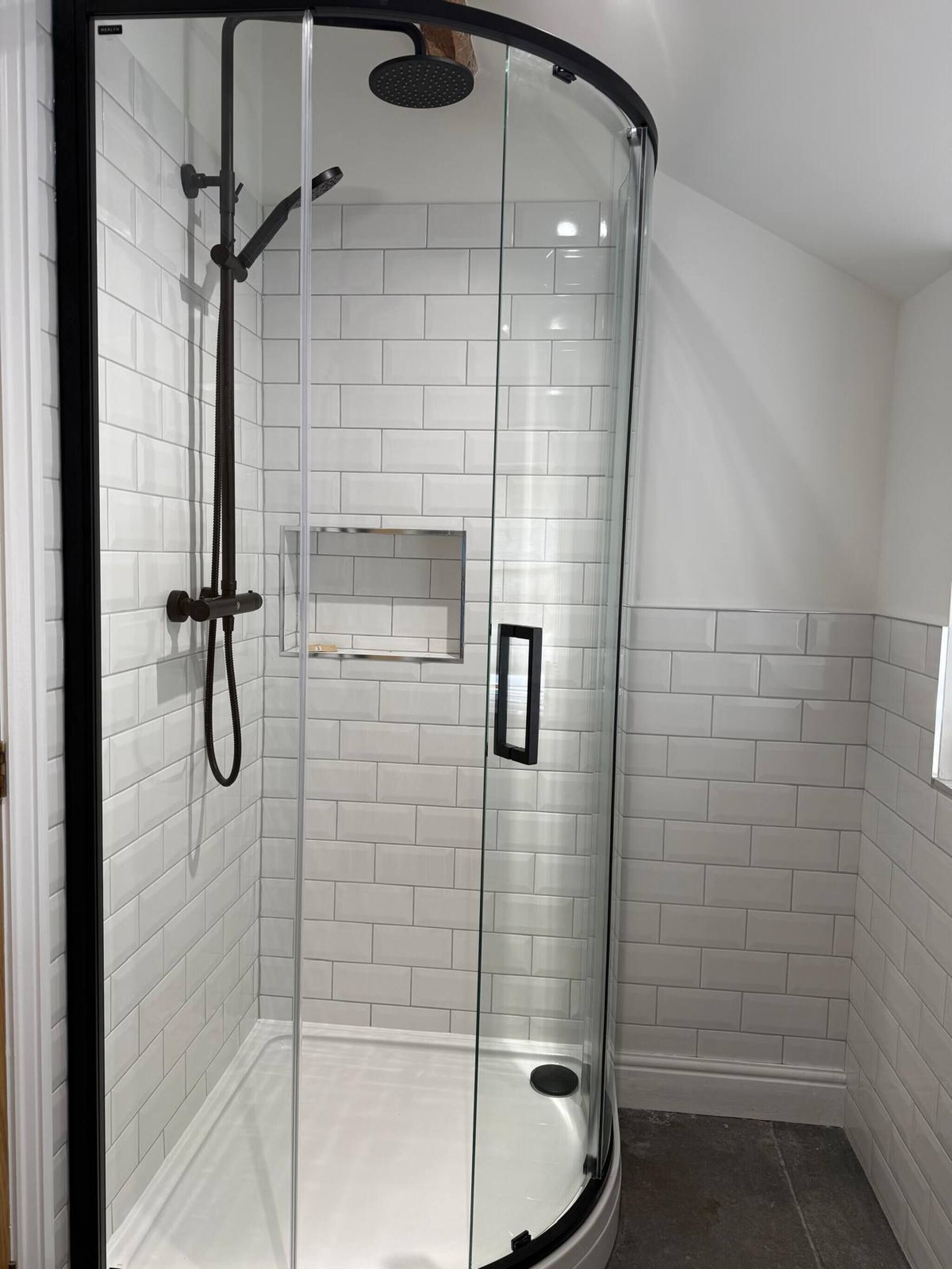 A glass-enclosed shower stall with white tiled walls and a black frame.