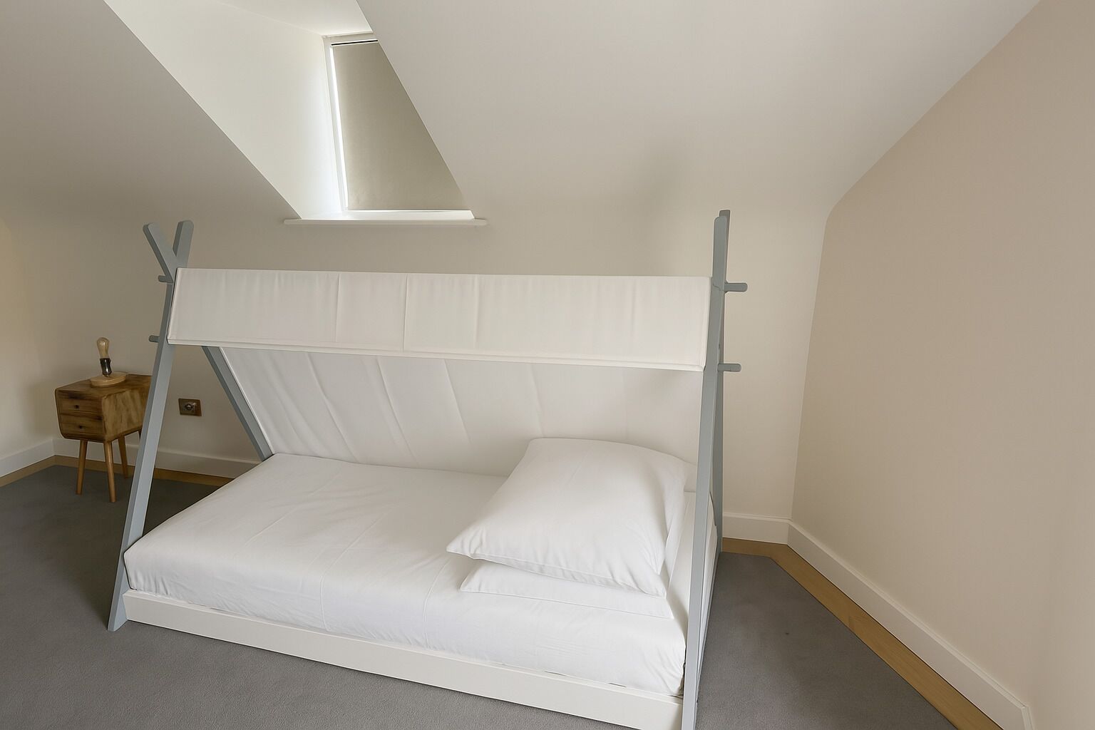 A single-bed room with a slanted ceiling, a small wooden nightstand, and a light bulb on it.