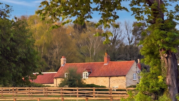 A rustic stone building with a red-tiled roof, a wooden fence, and a pond with swans. - Bridge House Modern Comfort in Historic Stone (Scarborough)