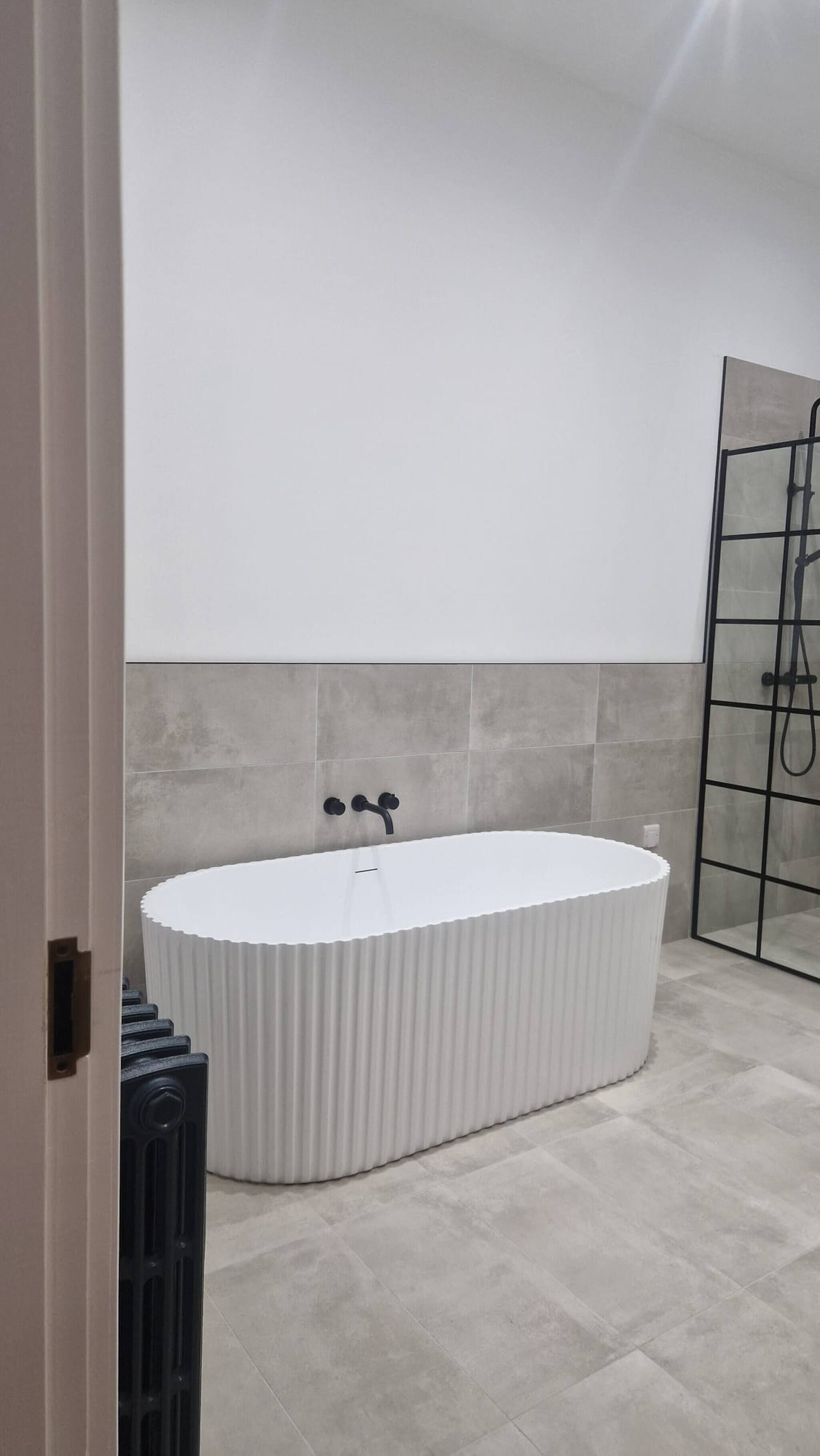 A modern bathroom with a freestanding bathtub, grey tiled walls, and a glass shower enclosure.