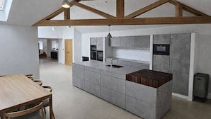 A modern kitchen with grey cabinetry, a wooden island, and exposed wooden beams. - Bridge House Modern Comfort in Historic Stone (Scarborough)