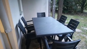 Ein rechteckiger Outdoor-Tisch mit sechs Stühlen, vor einer Wand mit Blick auf einen Garten.