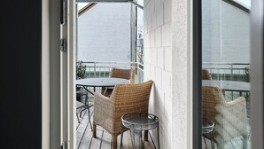 Ein Balkon mit Korbmöbeln, einer Glastür und Blick zum Himmel.