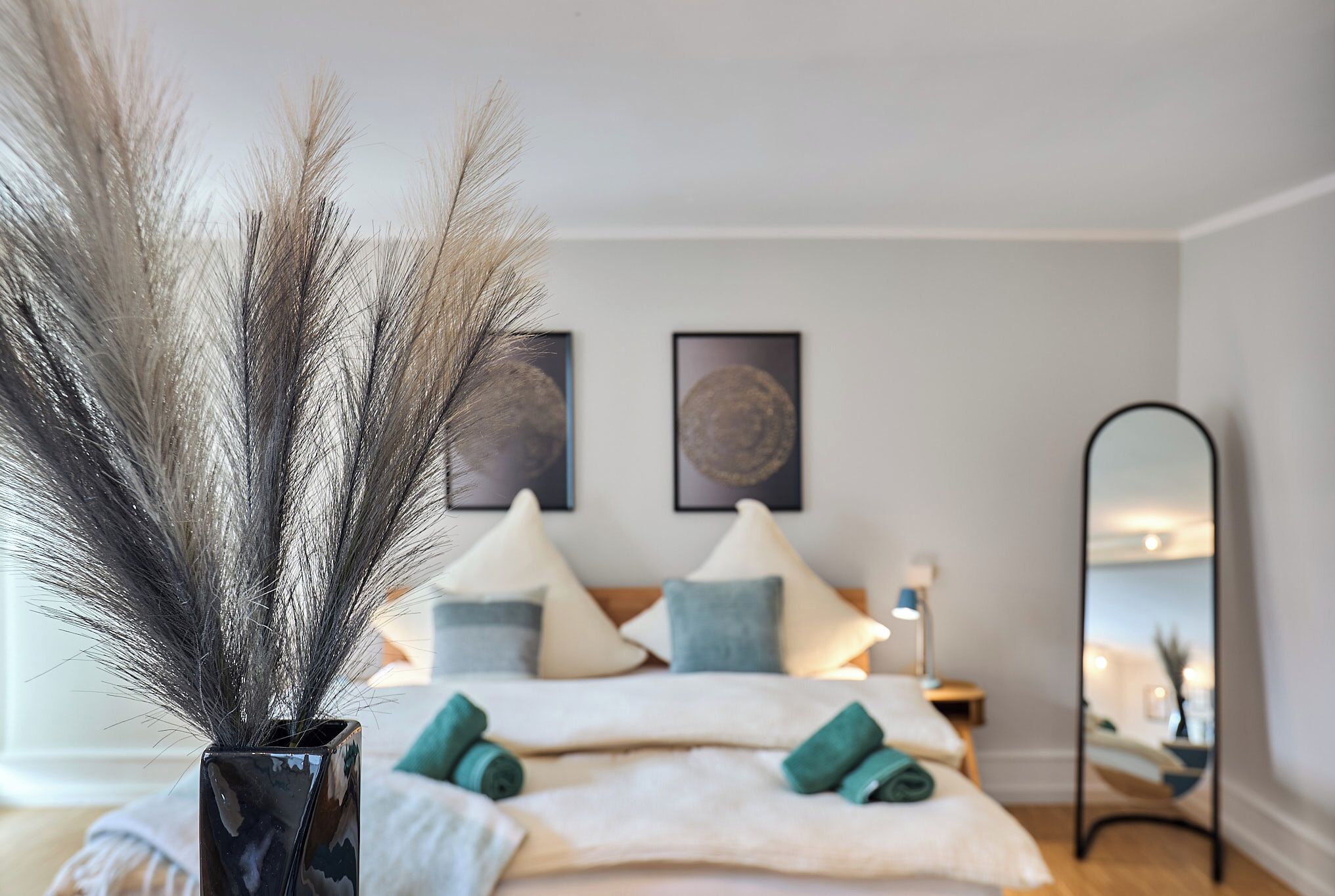 A bedroom with a bed, pillows, a bedside table, a mirror, and wall art.
