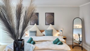 Ein Schlafzimmer mit Bett, Kissen, Nachttisch, Spiegel und Wandbildern.