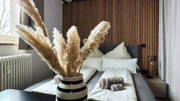 Une chambre moderne avec un lit, une table de chevet et un vase contenant de l’herbe des pampas.