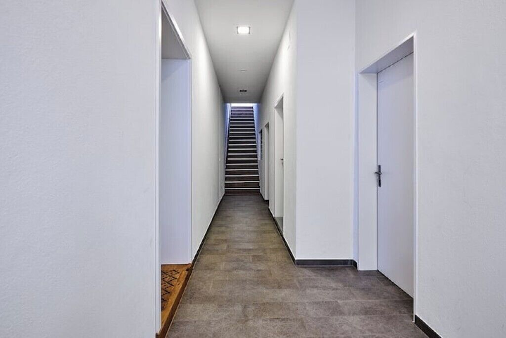 A narrow, well-lit hallway with a staircase at the end, leading to a door.