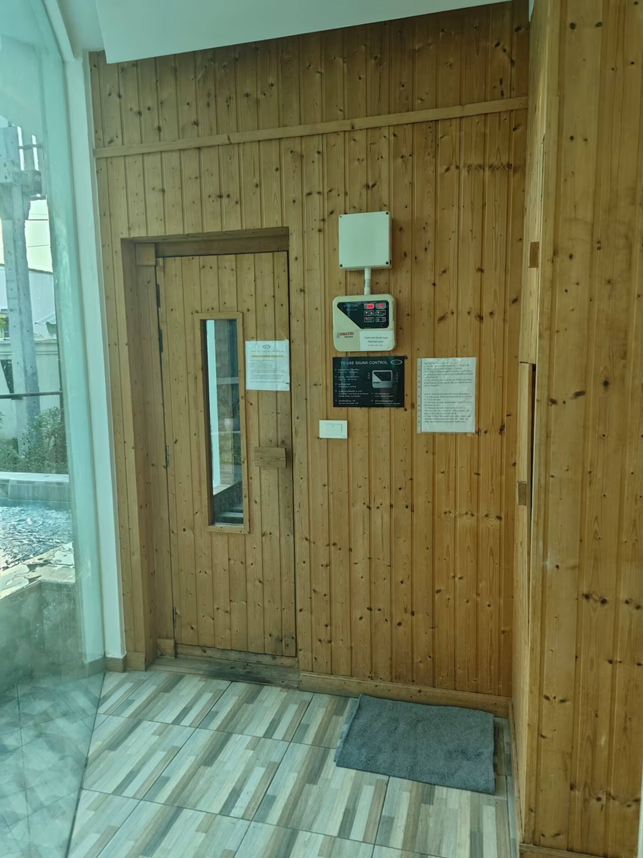 A wooden door with a control panel and informational signs, a glass window, and a tiled floor.