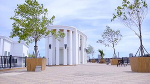 A spacious courtyard with a white building featuring columns, surrounded by trees and benches. - Resort Style Living - Great Location At Pattaya (Pattaya)