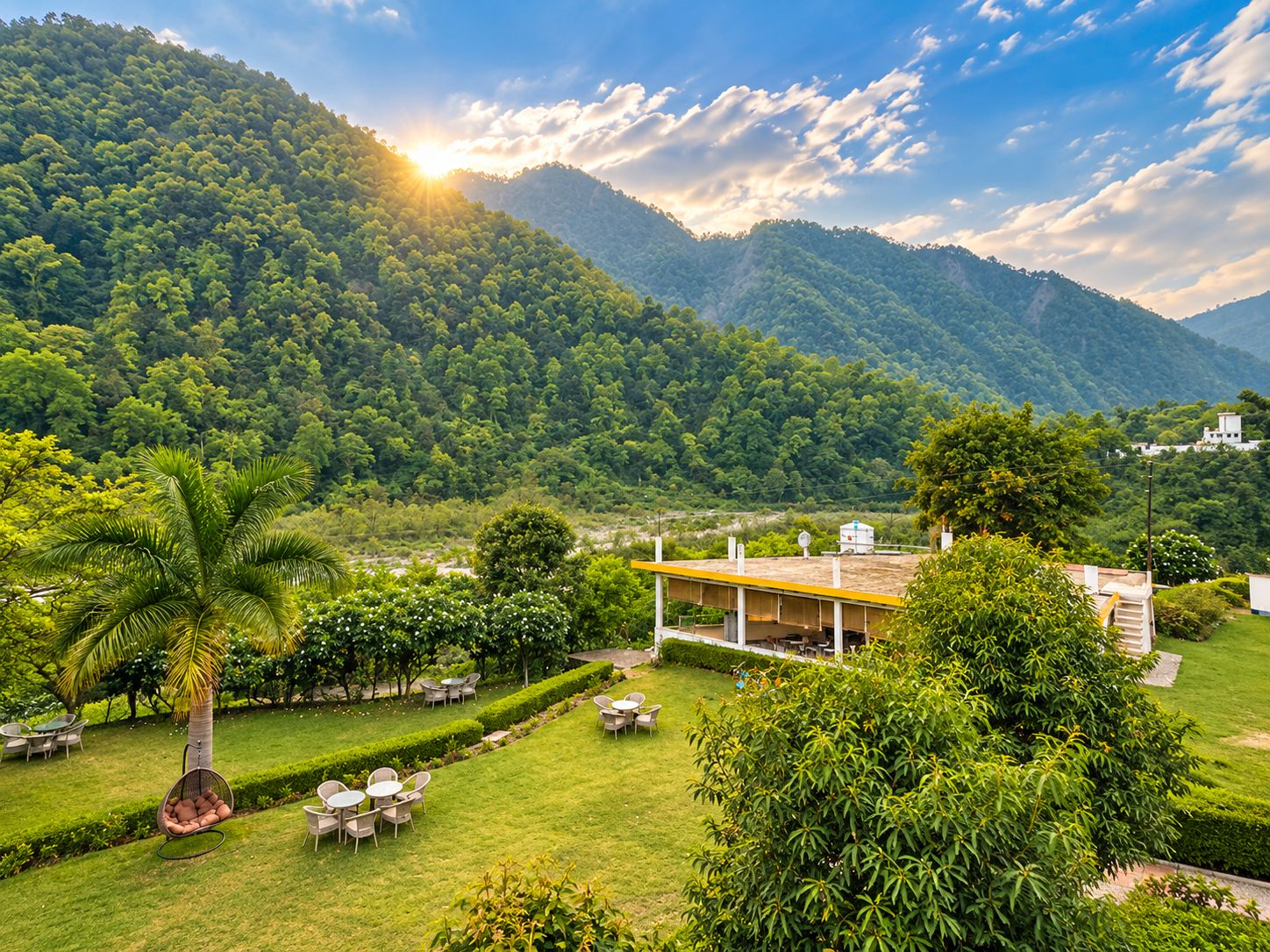 A lush green landscape with a building featuring outdoor seating and a view of a forested mountain.