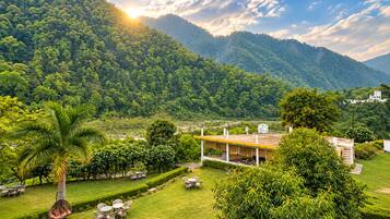 A lush green landscape with a building featuring outdoor seating and a view of a forested mountain.