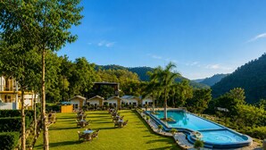 A resort with a swimming pool, outdoor seating, and a view of the surrounding hills. - Wild Vista Marchula Riverside Resort Jim Corbett (Marchula)